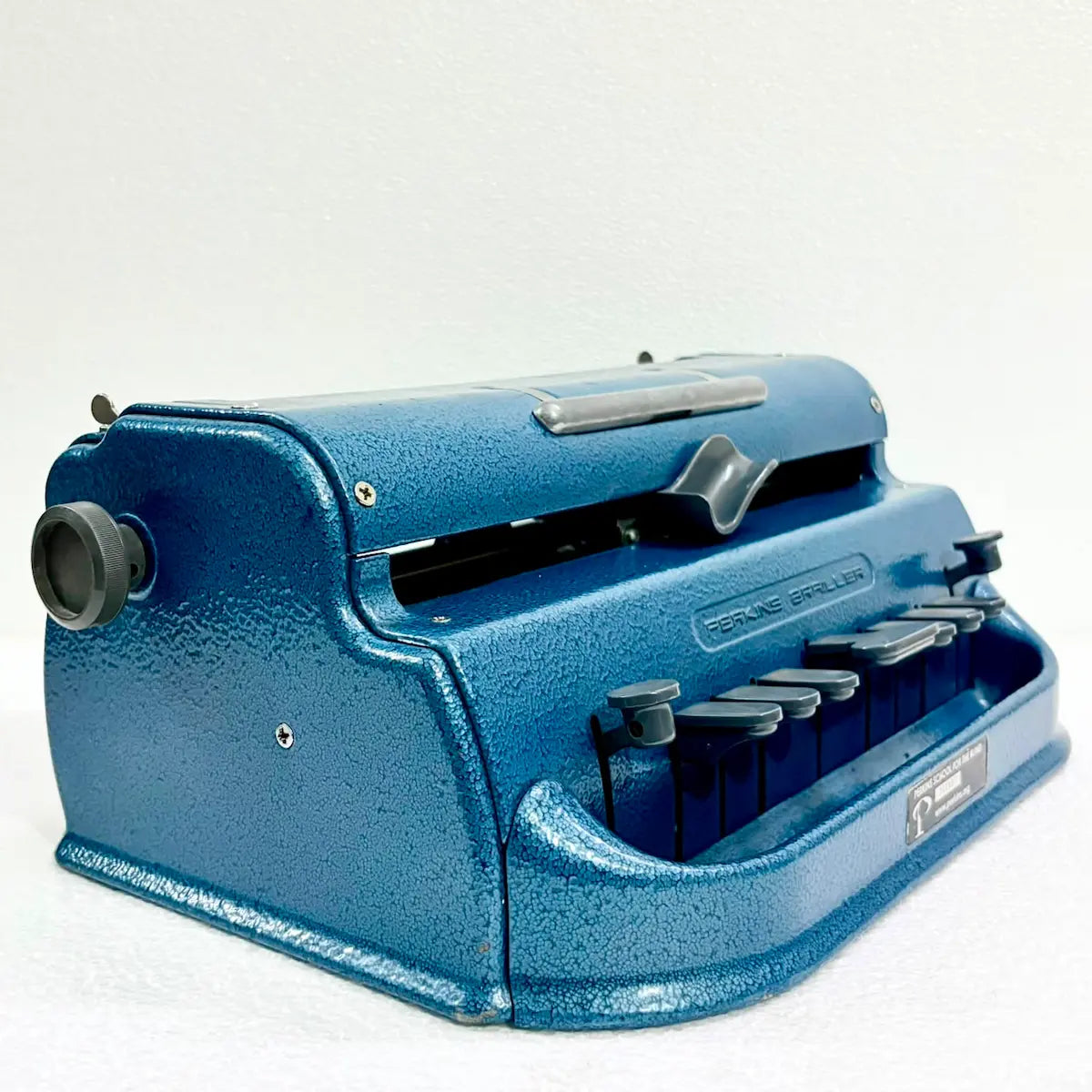 Three-quarter view of an original blue Perkins Braille Typewriter, a manual Braille typing machine from RR Typewriter Mart