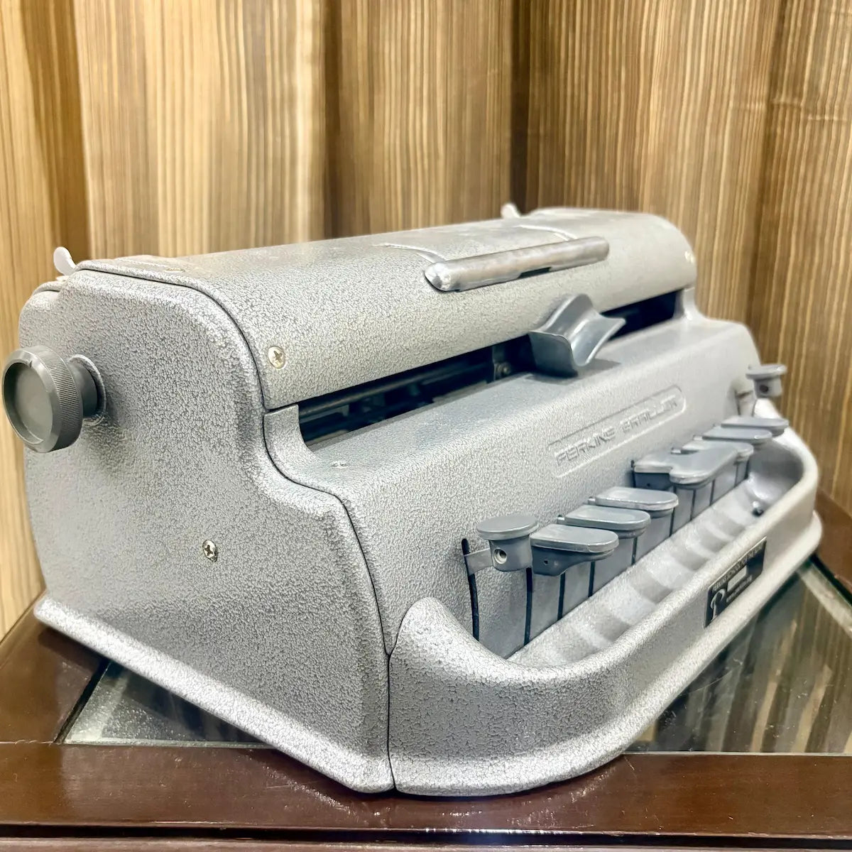 Side profile of the Perkins Brailler showing the platen knob and original grey factory finish at RR Typewriter Mart in India today.