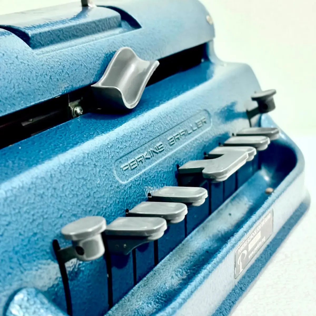 Close view of blue Perkins Brailler keys and textured body, showing a manual Braille typing machine from RR Typewriter Mart
