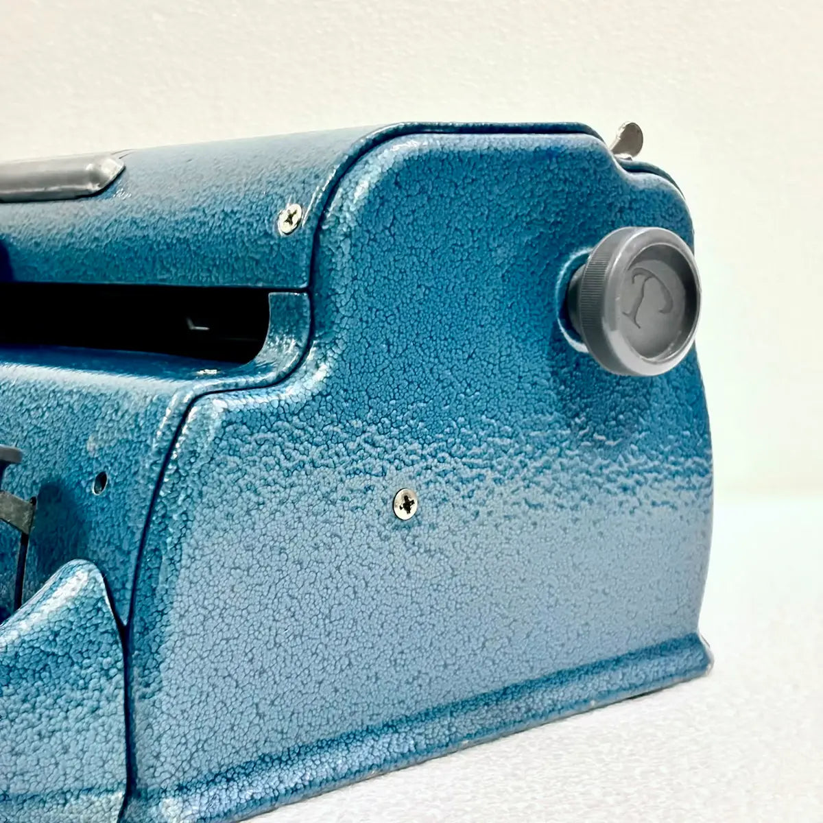 Close-up of a blue Perkins Braille Typewriter showing the carriage knob and textured metal body, a Perkins Brailler at RR Typewriter Mart