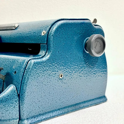 Close-up of a blue Perkins Braille Typewriter showing the carriage knob and textured metal body, a Perkins Brailler at RR Typewriter Mart