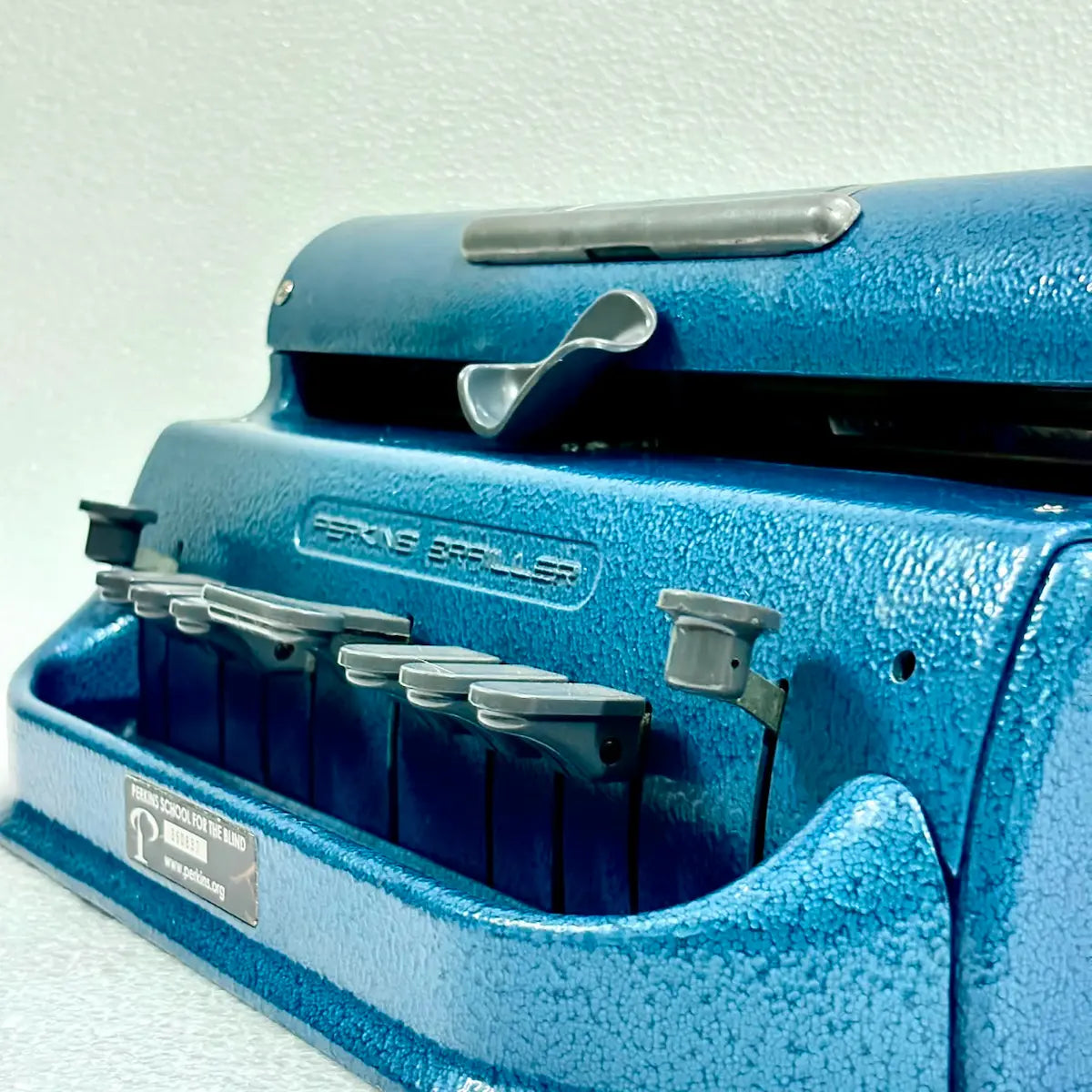 Close-up of blue Perkins Braille typing machine showing six keys and embossed logo, photographed by Perkins Braille Typewriter Seller RR Typewriter Mart