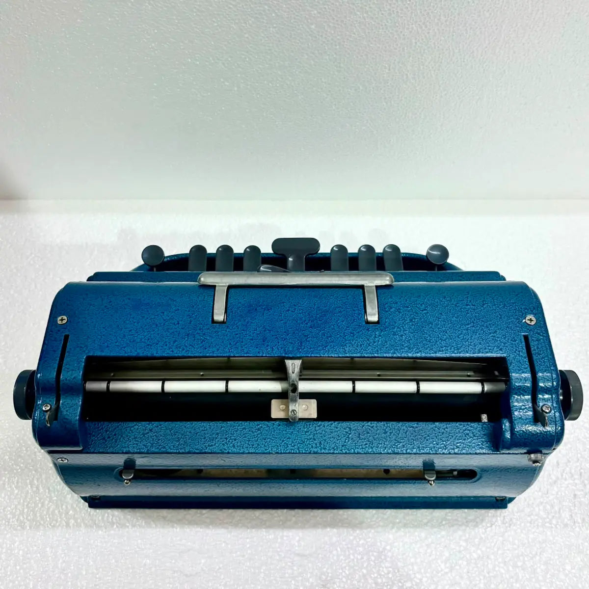 Rear view of a blue Perkins Braille Typewriter showing the paper roller and carriage mechanism, from RR Typewriter Mart.