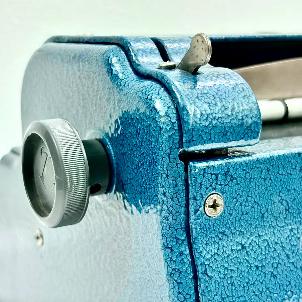 Close-up of blue Perkins Brailler adjustment knob and textured metal body, showing a manual Braille typing machine at RR Typewriter Mart.