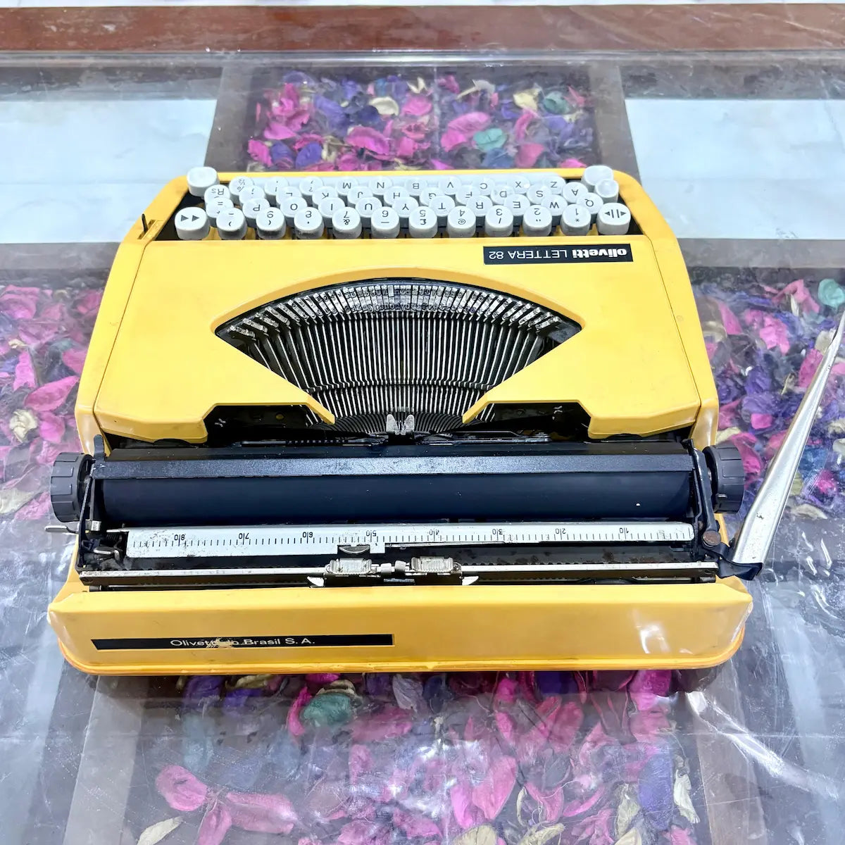 Rear overhead view of yellow Olivetti Lettera 82 Brazilian-made portable manual typewriter, showing carriage, platen and maker plate, RR Typewriter Mart