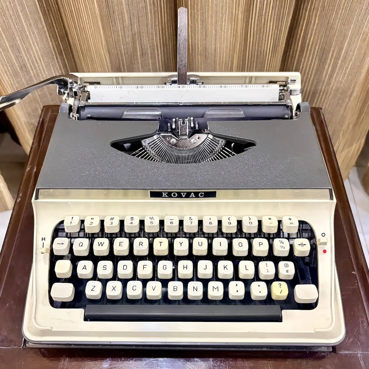 Kovac M-101A Japanese portable typewriter in original grey and ivory white, with cream keys and exposed typebars, photographed on a wooden table | RR Typewriter Mart