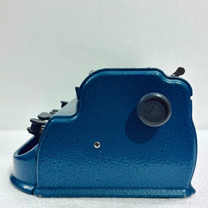 Side view of blue Perkins Braille Typewriter with adjustment knob, a manual braille typing machine from RR Typewriter Mart.