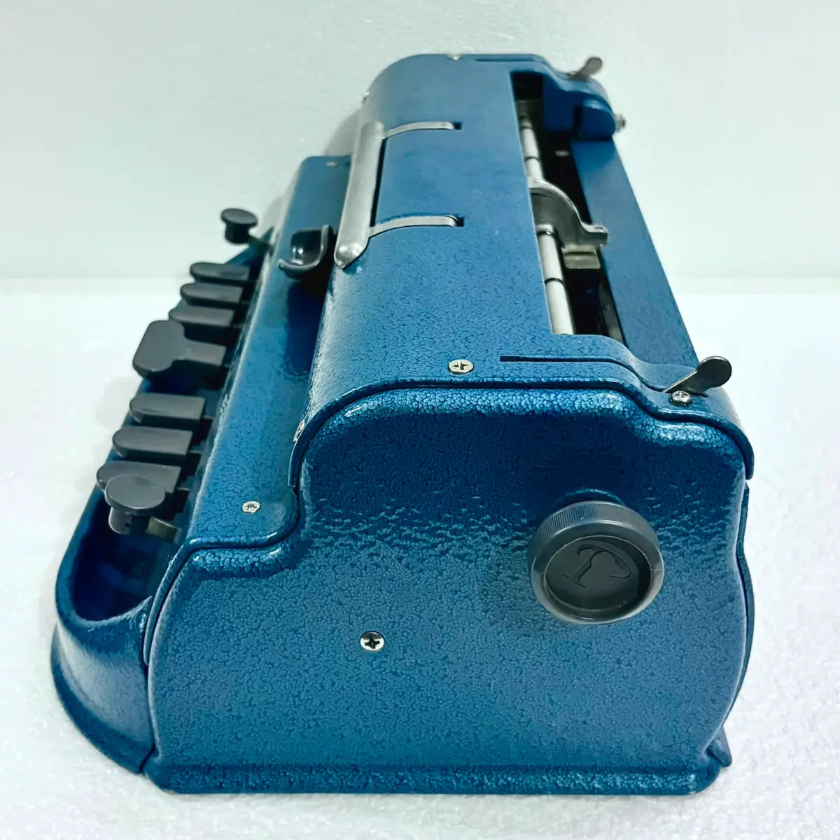 Angled rear view of blue Perkins Braille Typewriter with roller mechanism, a Perkins Brailler typewriter at RR Typewriter Mart.