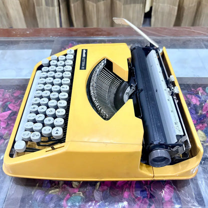Top-down angled view of Olivetti Lettera 82 yellow portable typewriter, showing English QWERTY keyboard, typebars and carriage, RR Typewriter Mart