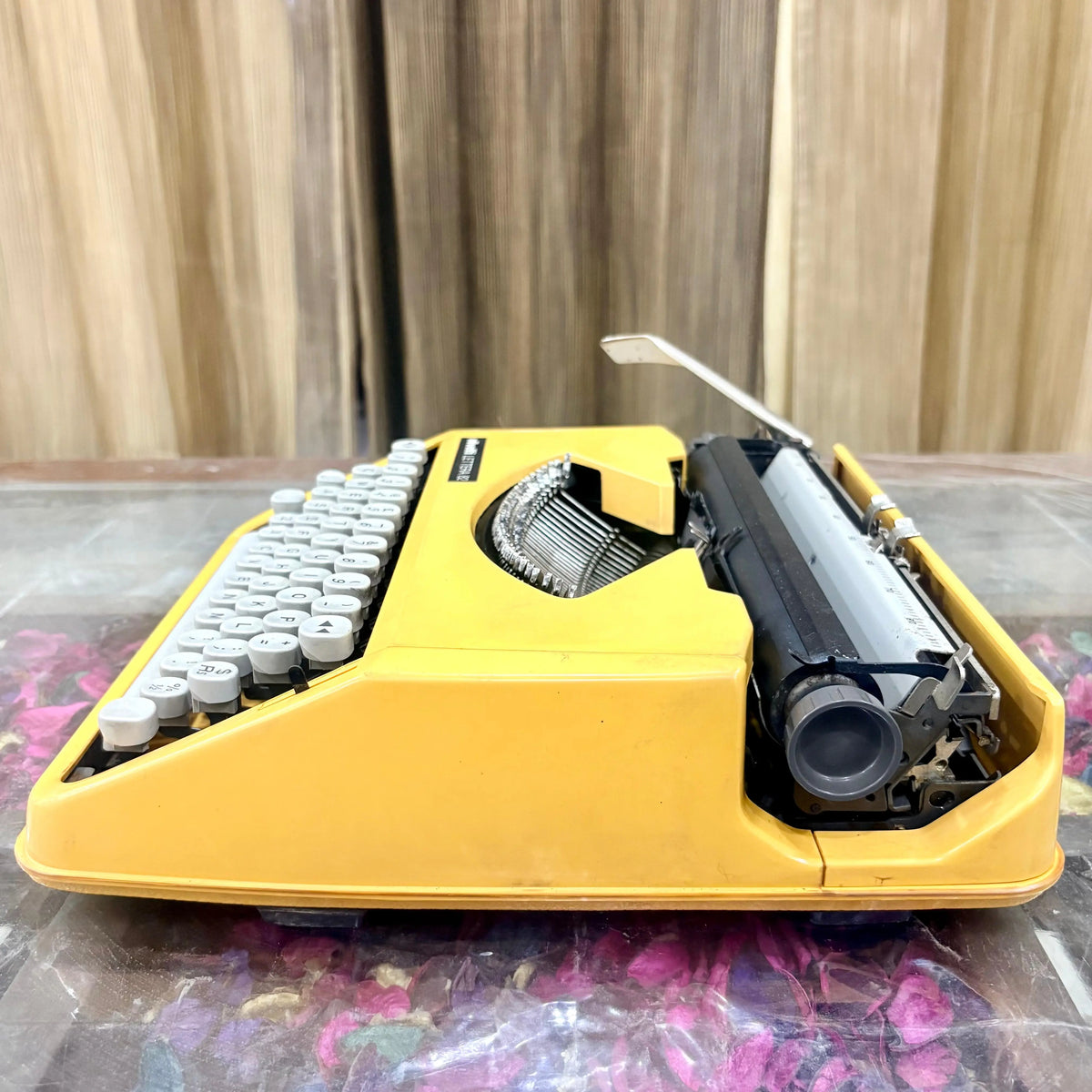 Angled side view of Olivetti Lettera 82 yellow portable manual typewriter, showing white QWERTY keys, black platen and carriage, RR Typewriter Mart