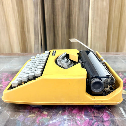 Angled side view of Olivetti Lettera 82 yellow portable manual typewriter, showing white QWERTY keys, black platen and carriage, RR Typewriter Mart