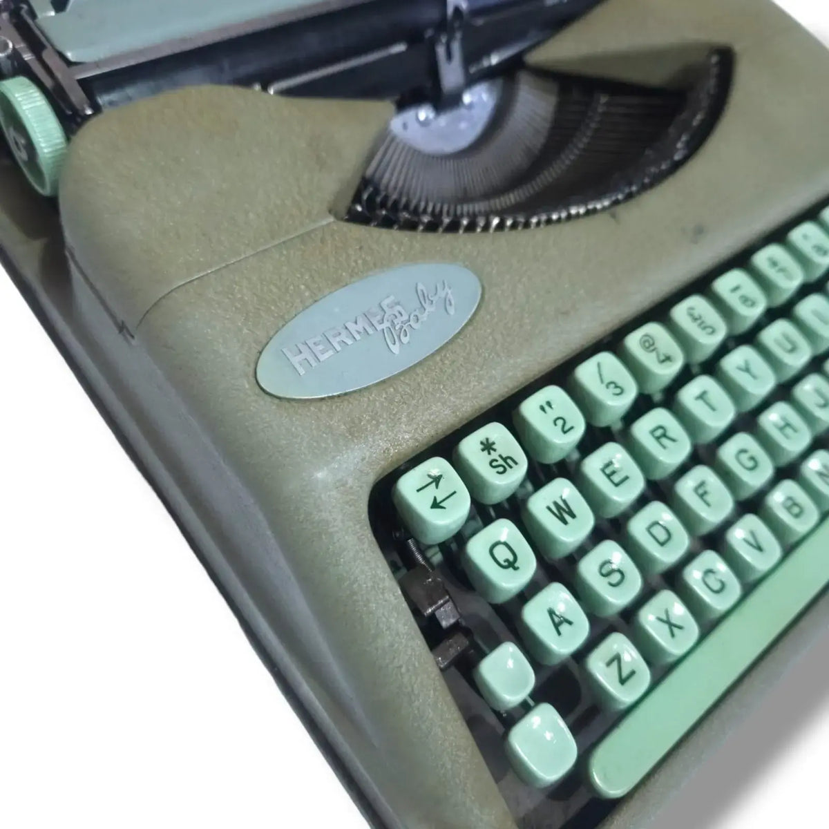 Hermes Baby Rocket typewriter close-up showing original badge, mint green keys and exposed Swiss typing mechanism