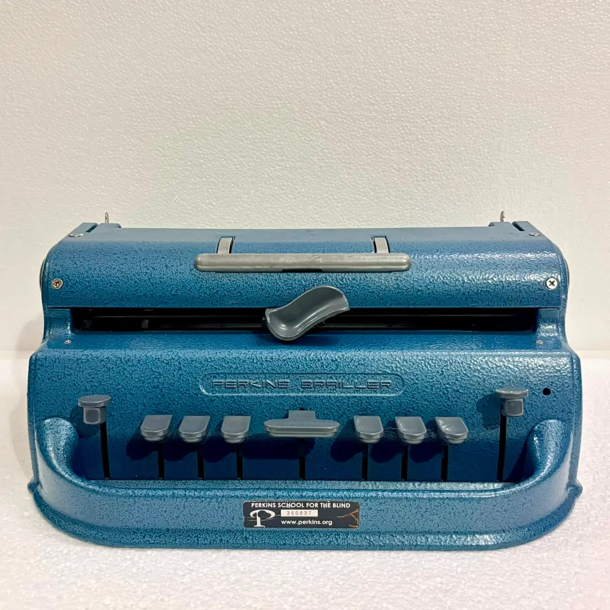 Front view of an original blue Perkins Braille Typewriter with six-key layout and textured finish, photographed by RR Typewriter Mart