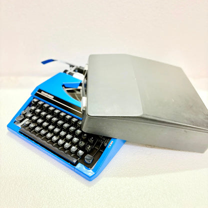 Silver Reed Silverette II blue portable typewriter placed beside grey carry case, an English manual typewriter