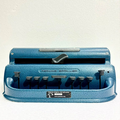 Front view of a blue Perkins Braille Typewriter showing six Braille keys and textured metal body, photographed by RR Typewriter Mart